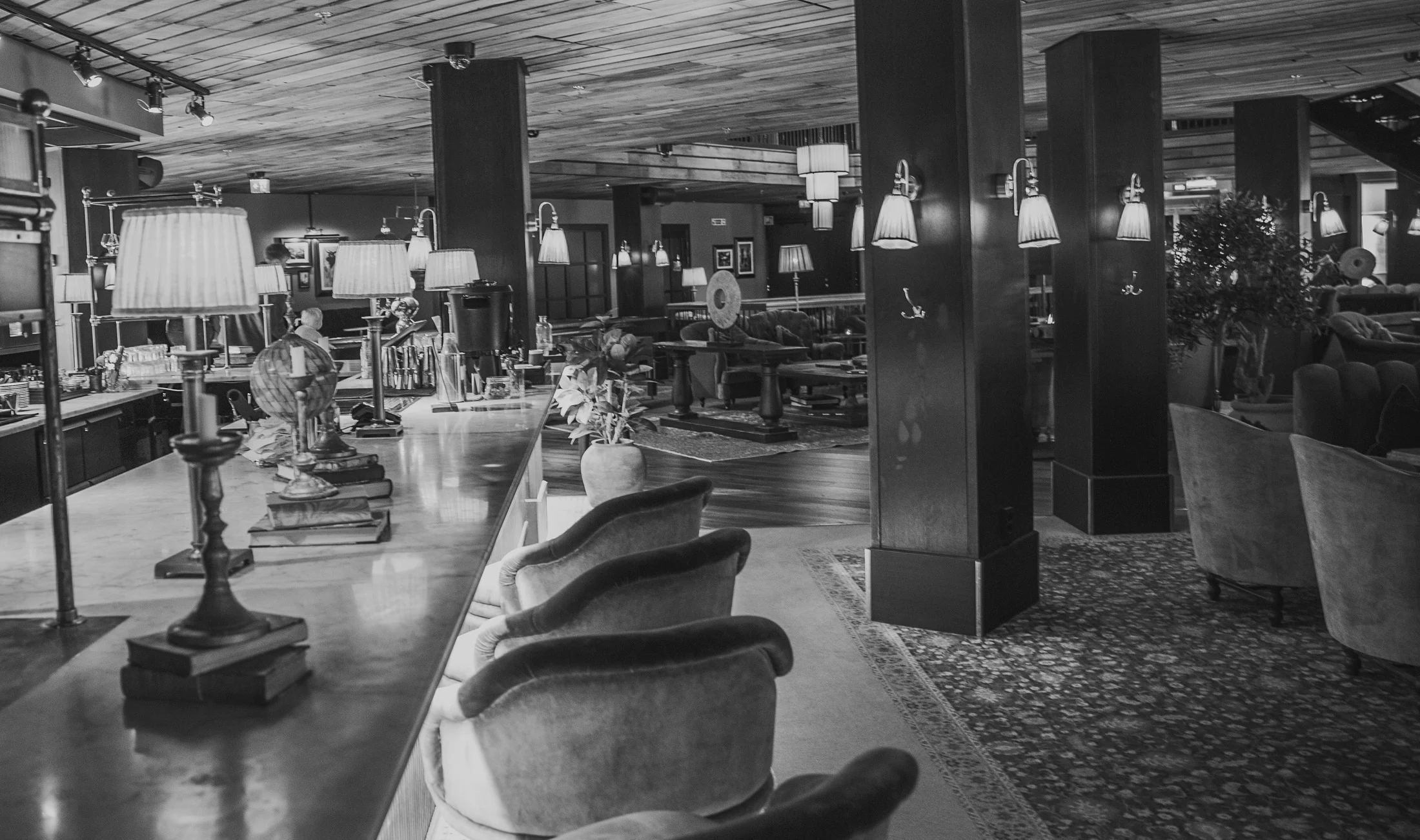 Elegant hotel lounge with a marble bar, table lamps, upholstered chairs, sofas, and wood-paneled columns