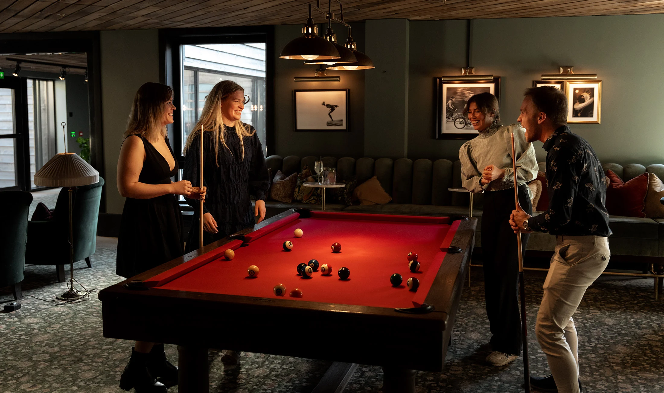 Four people play pool in a warmly lit lounge