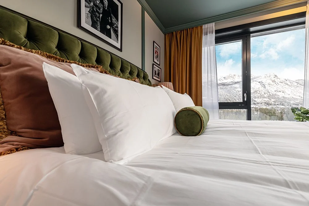 Standard_Double_Mountain_View_Fyri_Resort Bedroom with white bedding, green velvet headboard, and a mountain view through the window