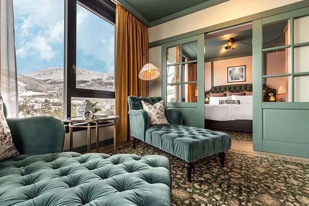 Suite_Fyri_Resort Room with teal velvet seating, a bed, and snowy mountain views through large windows