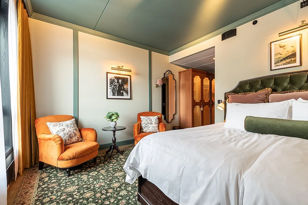 Superior_Double_Fyri_Resort Elegant hotel bedroom with a large bed, orange armchairs, floral carpet, and vintage furnishings