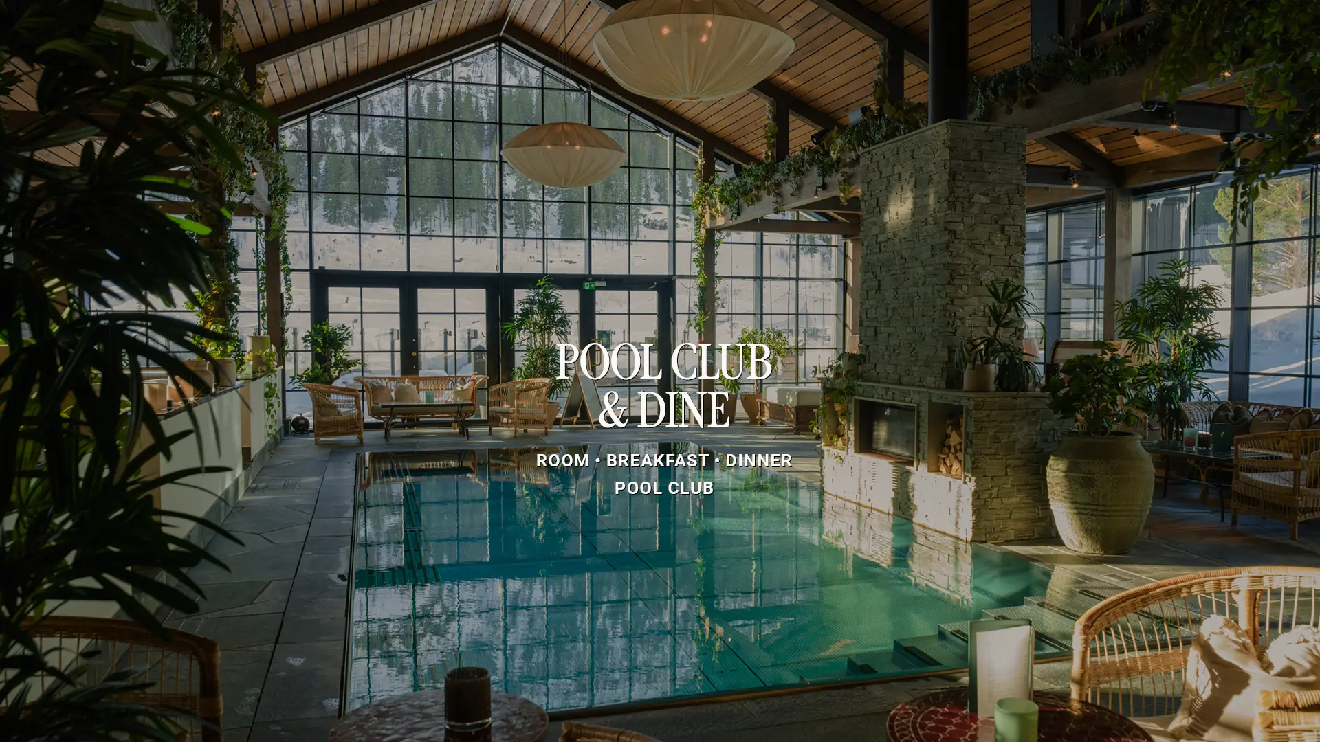 Fyri-Paket-BV-26-POOL CLUB & DINE Indoor pool surrounded by large windows overlooking a snowy forest, with a stone fireplace, plants and wicker furniture. Text overlay: “Pool Club & Dine – Room, Breakfast, Dinner, Pool Club”.