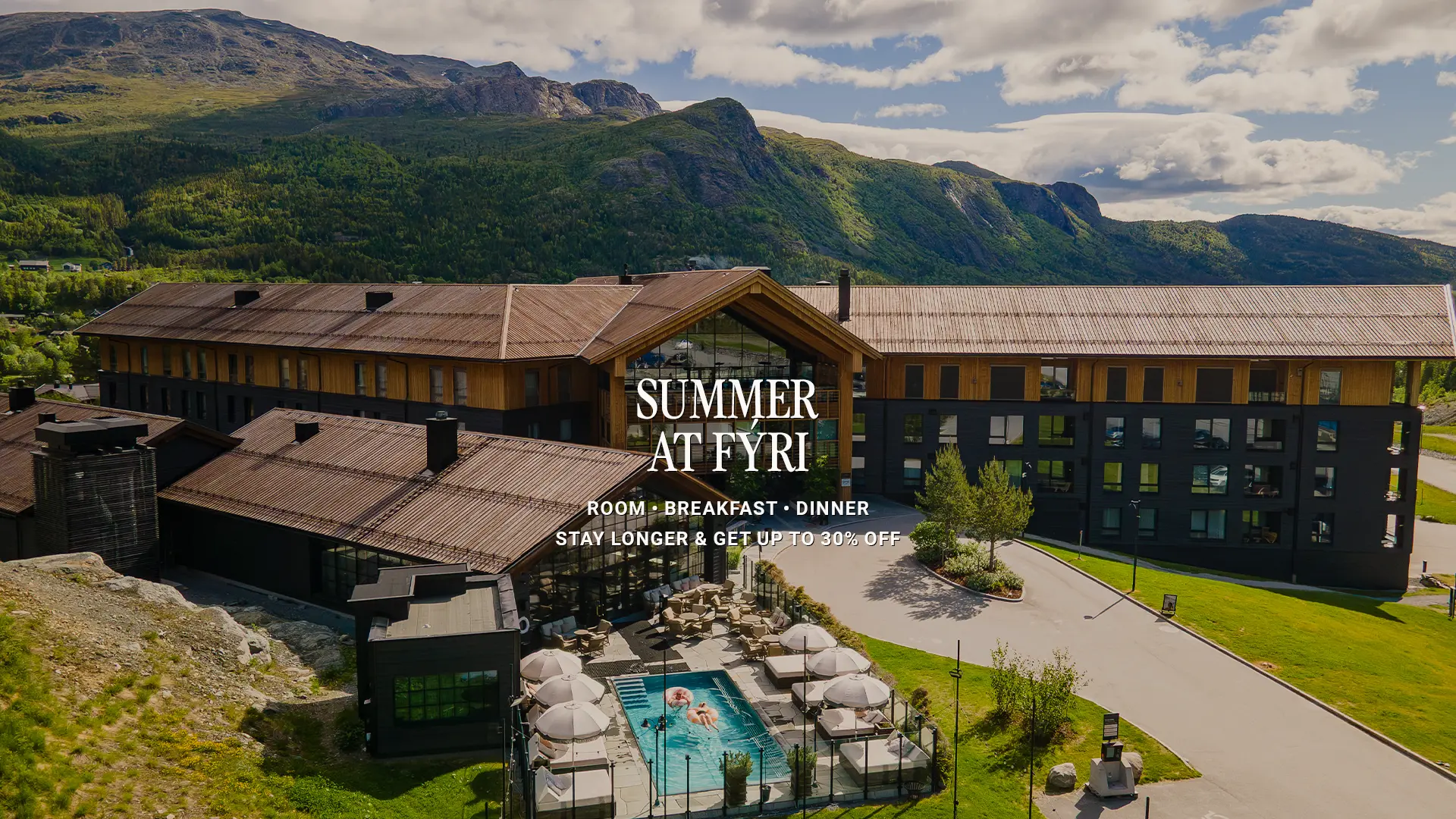 Fyri-Paket-BV-26-SIGNATURE STAY-NY Aerial view of Fýri Hotel on a summer day, with an outdoor pool, parasols and green mountains behind. Text overlay: “Summer at Fýri – Room, Breakfast, Dinner, Stay longer & get up to 30% off”.